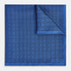 The Geometric Blue Pocket Square in Silk by Turnbull & Asser UK features a vibrant blue design adorned with small, outlined squares arranged in a grid of sharp navy lines. One corner is neatly folded to reveal the reverse side, with "Turnbull & Asser" printed at the bottom right.
