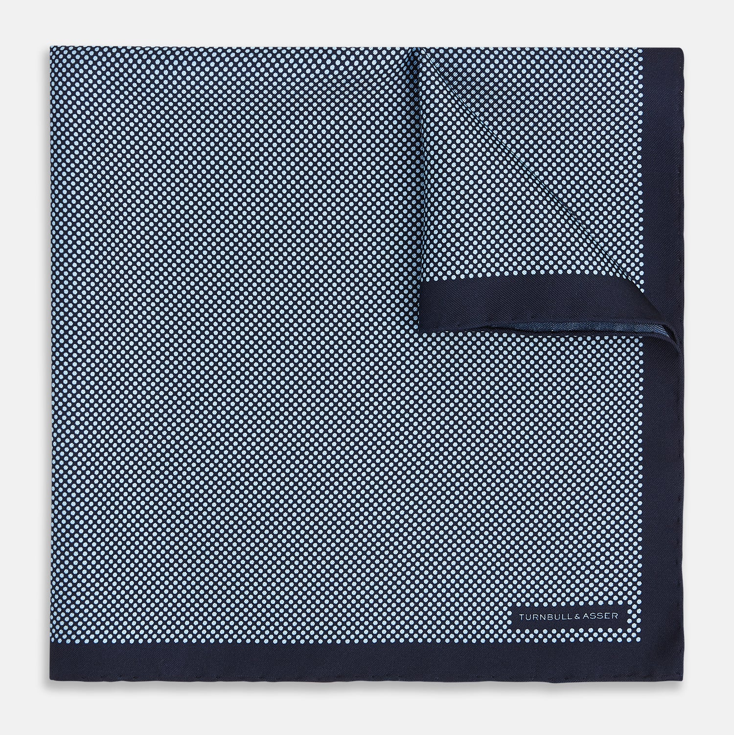 View 1 of product Introducing the Polka Dot Navy Pocket Square in Silk by Turnbull & Asser UK—this elegant accessory features a refined dot motif with small white polka dots and a solid navy border. One corner is artfully folded to reveal the underside, adding visual interest, while the Turnbull & Asser branding is printed in white on one corner, making it an ideal choice for formal tailoring.