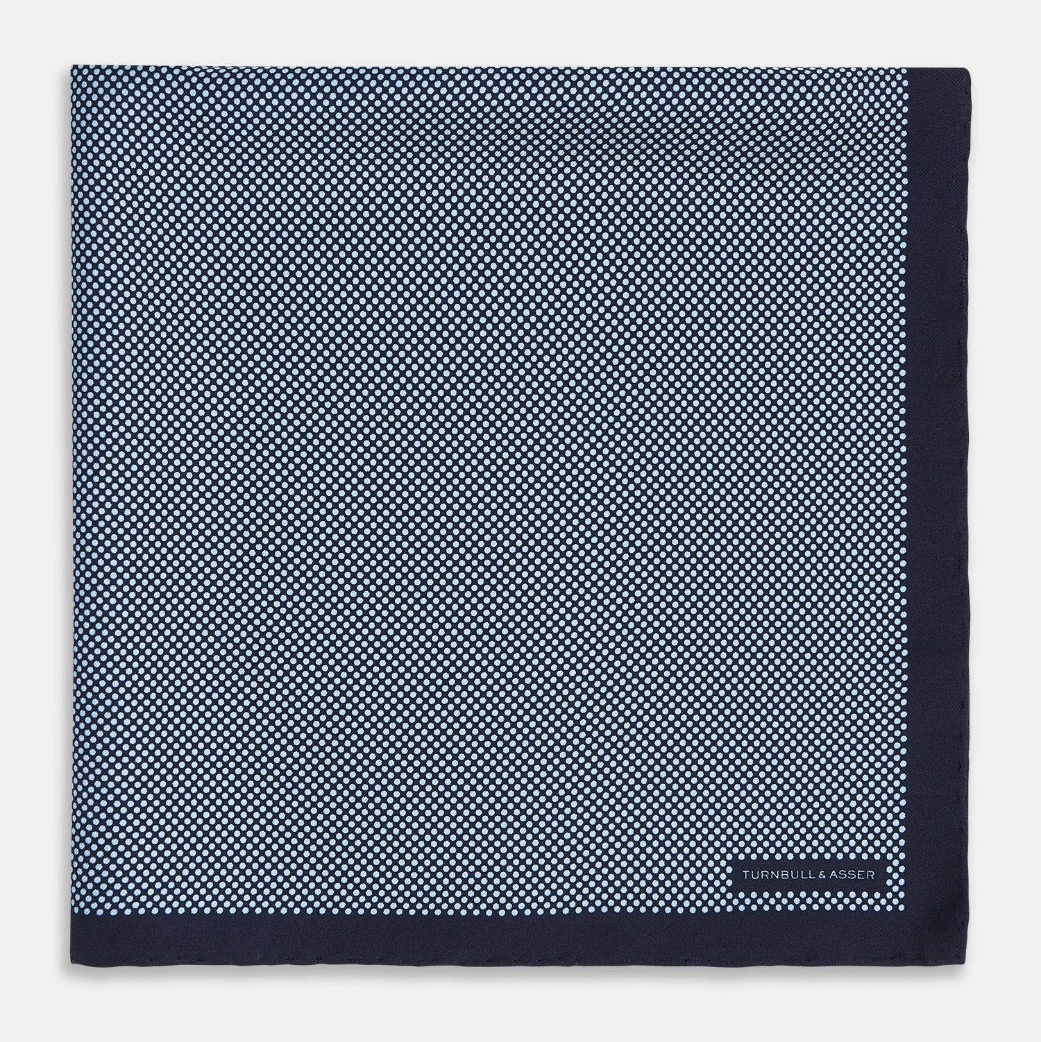 View 3 of product Introducing the Polka Dot Navy Pocket Square in Silk by Turnbull & Asser UK—this elegant accessory features a refined dot motif with small white polka dots and a solid navy border. One corner is artfully folded to reveal the underside, adding visual interest, while the Turnbull & Asser branding is printed in white on one corner, making it an ideal choice for formal tailoring.