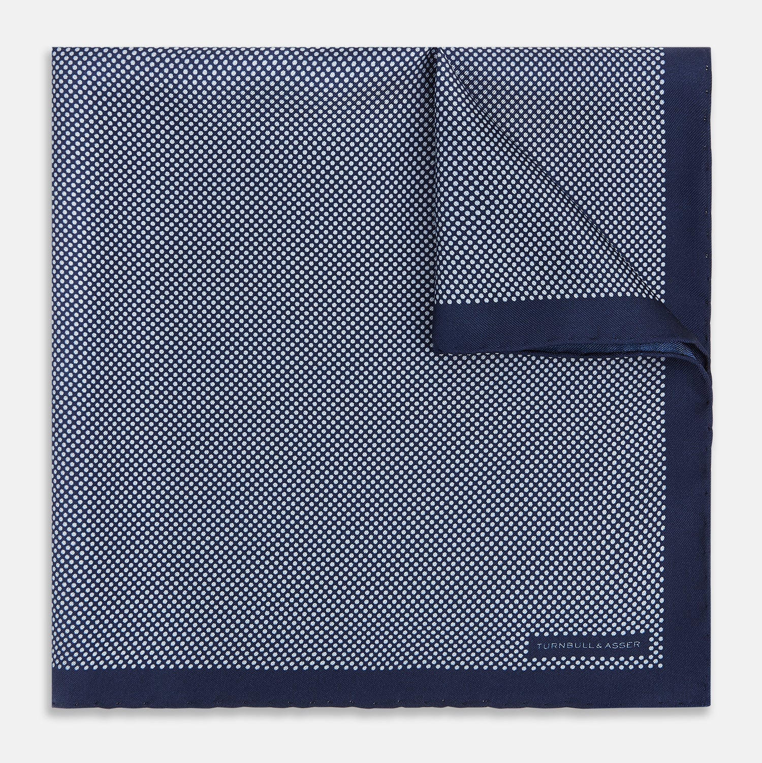View 1 of product Crafted from silk, the Turnbull & Asser UK Polka dot Denim Pocket Square features a sophisticated navy blue hue adorned with small white polka dots and a solid border. Neatly folded with the brand label visible in one corner, this elegant accessory is ideal for enhancing formal tailoring.