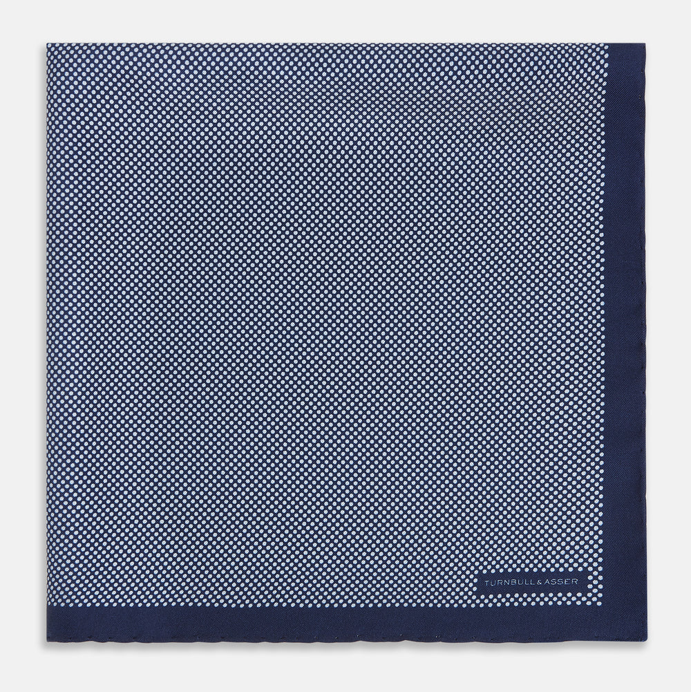 Crafted from silk, the Turnbull & Asser UK Polka dot Denim Pocket Square features a sophisticated navy blue hue adorned with small white polka dots and a solid border. Neatly folded with the brand label visible in one corner, this elegant accessory is ideal for enhancing formal tailoring.