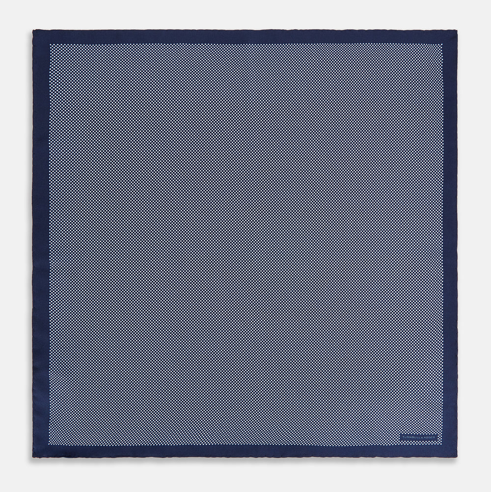 Crafted from silk, the Turnbull & Asser UK Polka dot Denim Pocket Square features a sophisticated navy blue hue adorned with small white polka dots and a solid border. Neatly folded with the brand label visible in one corner, this elegant accessory is ideal for enhancing formal tailoring.