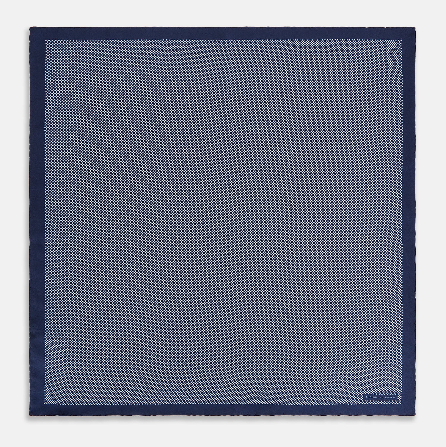 View 4 of product Crafted from silk, the Turnbull & Asser UK Polka dot Denim Pocket Square features a sophisticated navy blue hue adorned with small white polka dots and a solid border. Neatly folded with the brand label visible in one corner, this elegant accessory is ideal for enhancing formal tailoring.