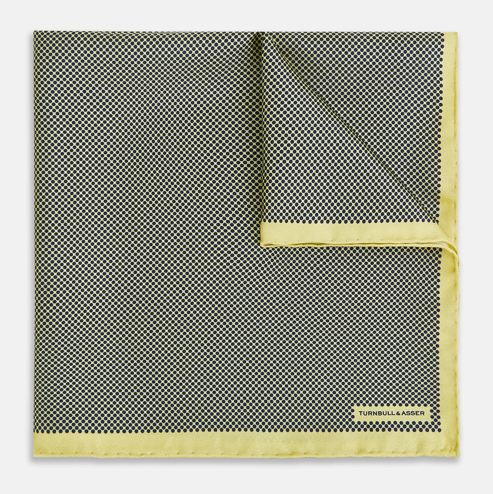 A folded yellow silk pocket square with a subtle polka dot pattern and yellow edges, perfect for formal tailoring. The Turnbull & Asser UK label is visible in one corner.