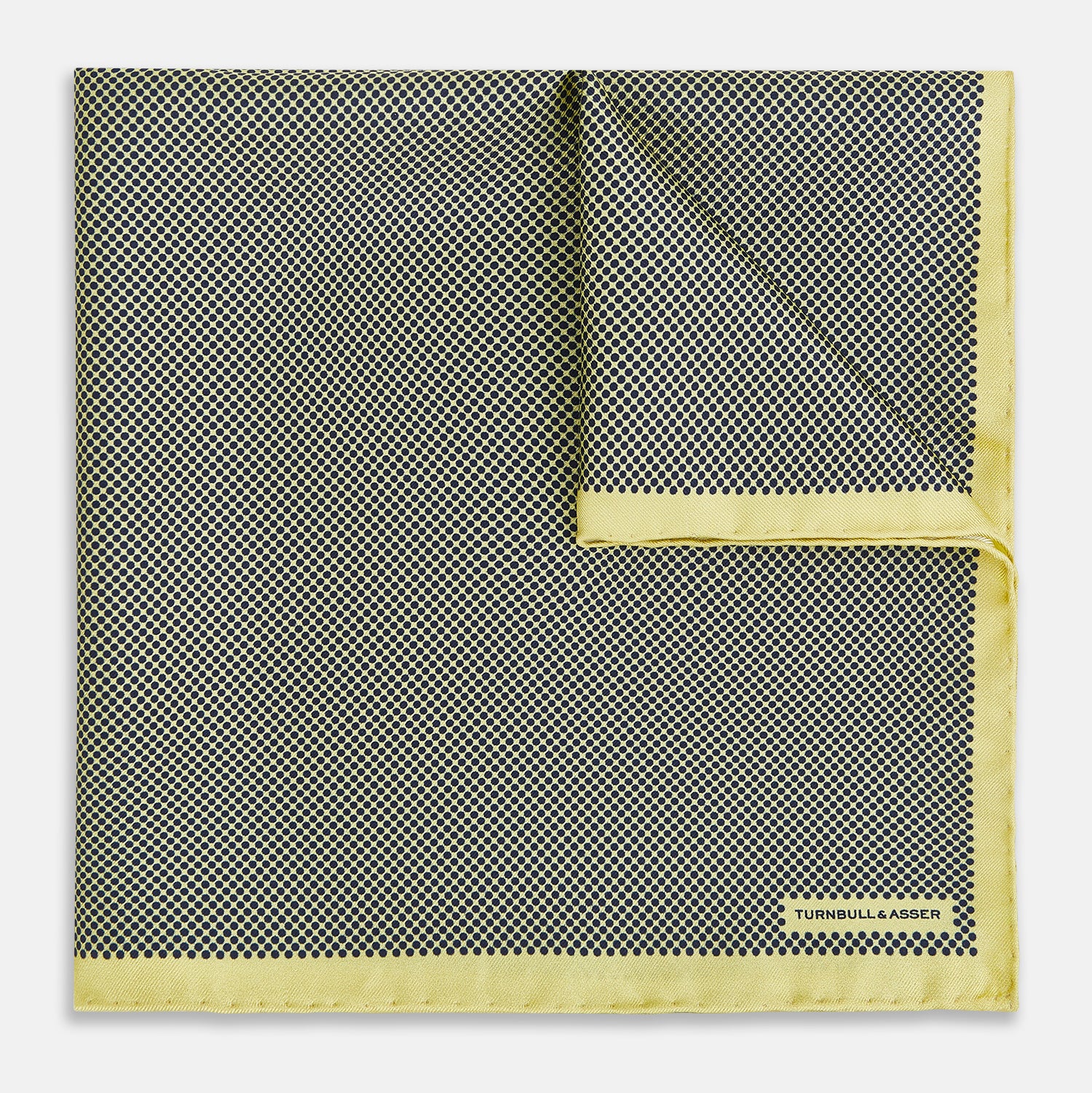 View 1 of product A folded yellow silk pocket square with a subtle polka dot pattern and yellow edges, perfect for formal tailoring. The Turnbull & Asser UK label is visible in one corner.