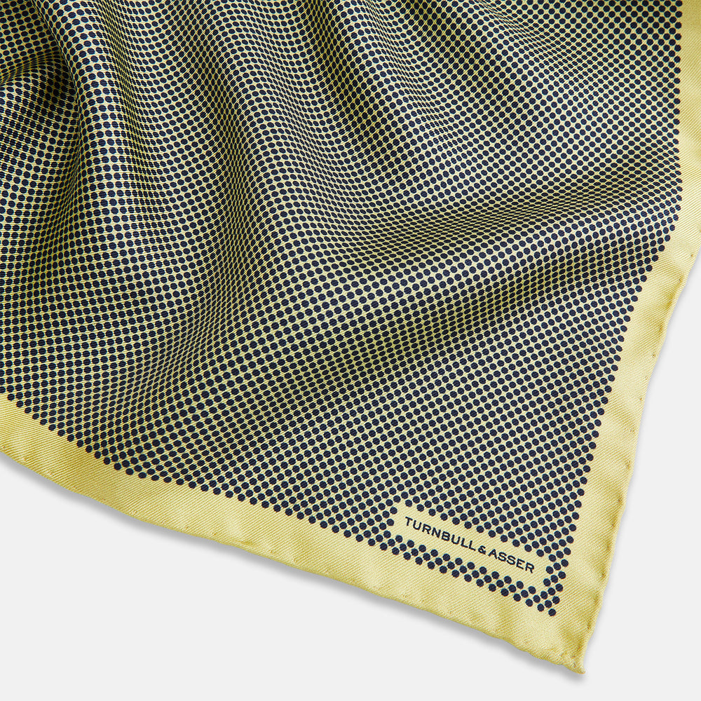 A folded yellow silk pocket square with a subtle polka dot pattern and yellow edges, perfect for formal tailoring. The Turnbull & Asser UK label is visible in one corner.