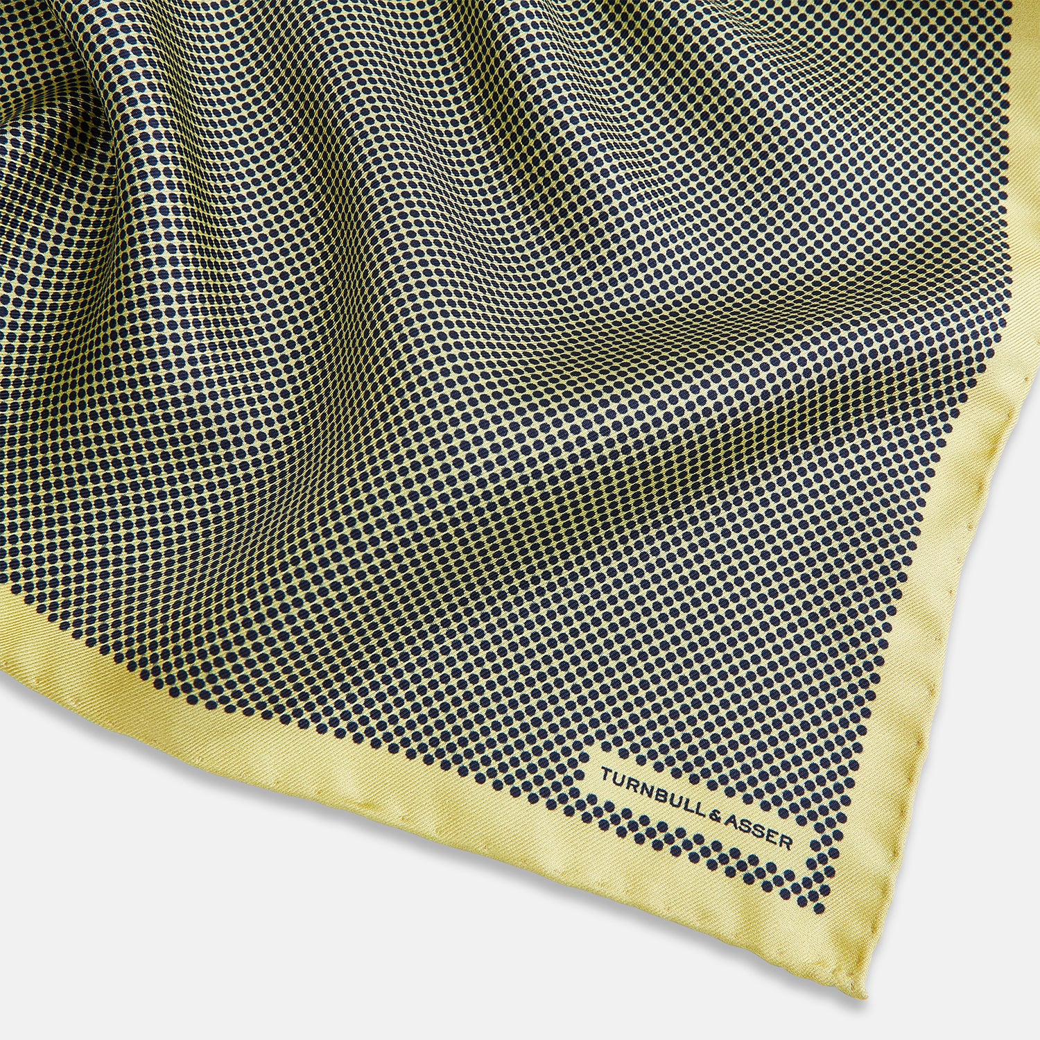 View 2 of product A folded yellow silk pocket square with a subtle polka dot pattern and yellow edges, perfect for formal tailoring. The Turnbull & Asser UK label is visible in one corner.