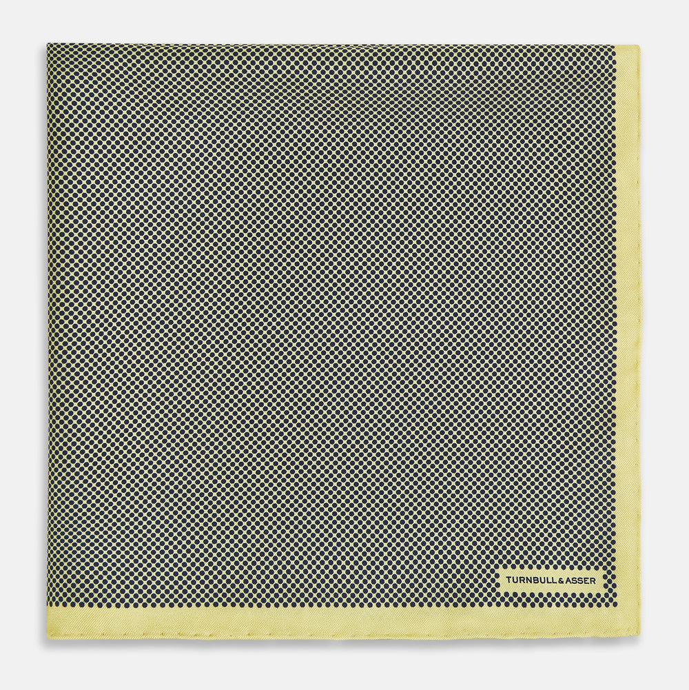 A folded yellow silk pocket square with a subtle polka dot pattern and yellow edges, perfect for formal tailoring. The Turnbull & Asser UK label is visible in one corner.