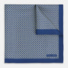 View 1 of product A blue pocket square from Turnbull & Asser UK, featuring a geometric white square pattern and a solid blue border. One corner is folded to highlight the striking design on both sides, with the brand name displayed on the bottom right. Product name: POCKET SQUARE SQUARE PATTERNED BANANA.