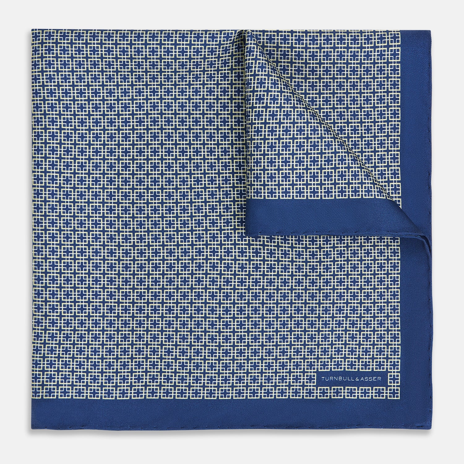 View 1 of product A blue pocket square from Turnbull & Asser UK, featuring a geometric white square pattern and a solid blue border. One corner is folded to highlight the striking design on both sides, with the brand name displayed on the bottom right. Product name: POCKET SQUARE SQUARE PATTERNED BANANA.