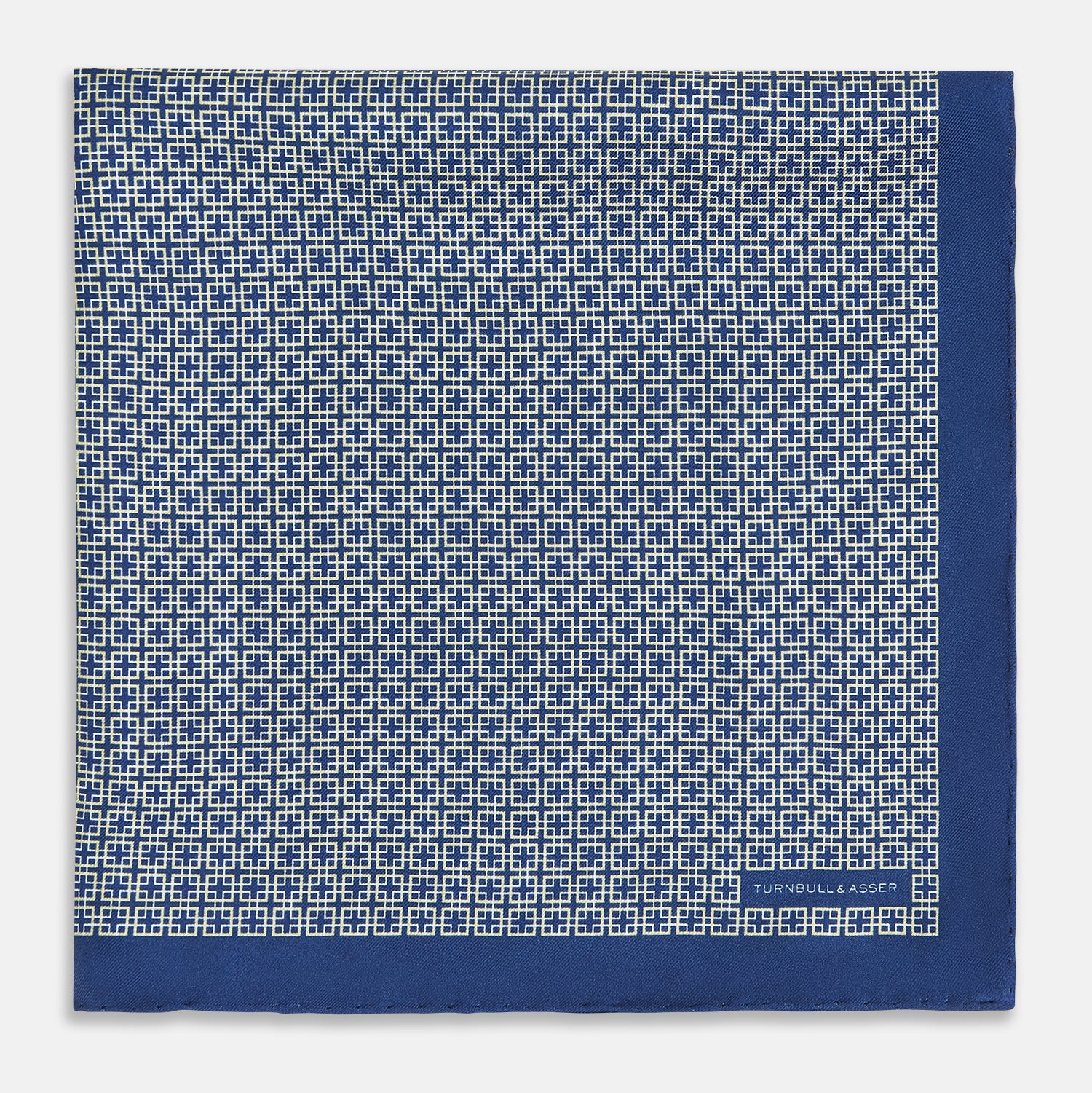 View 3 of product A blue pocket square from Turnbull & Asser UK, featuring a geometric white square pattern and a solid blue border. One corner is folded to highlight the striking design on both sides, with the brand name displayed on the bottom right. Product name: POCKET SQUARE SQUARE PATTERNED BANANA.