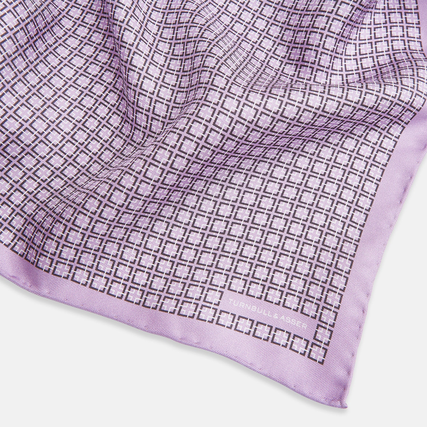 View 2 of product Crafted by Turnbull & Asser UK, the Geometric Lilac Pocket Square in Silk features an elegant square pattern in lilac hues, accented by a solid lavender border. When folded, it tastefully displays a glimpse of the sophisticated patterned underside.
