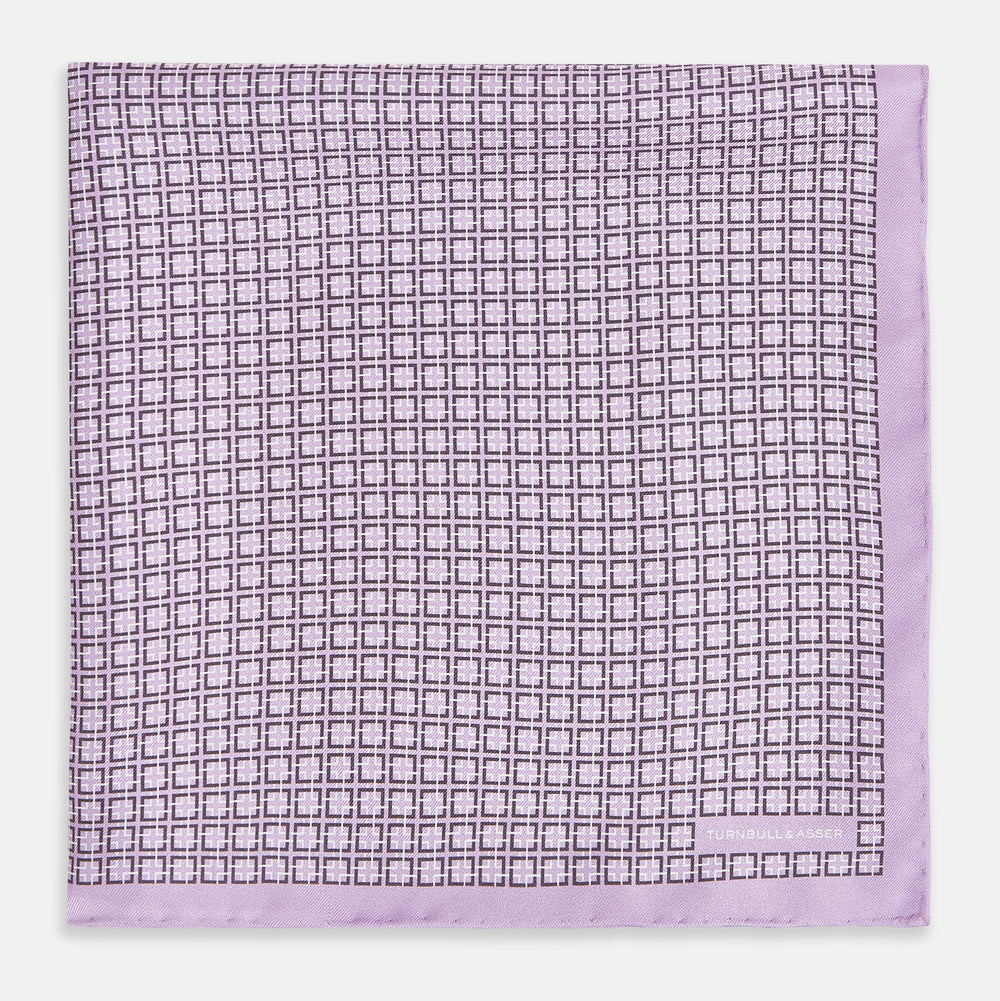 Crafted by Turnbull & Asser UK, the Geometric Lilac Pocket Square in Silk features an elegant square pattern in lilac hues, accented by a solid lavender border. When folded, it tastefully displays a glimpse of the sophisticated patterned underside.