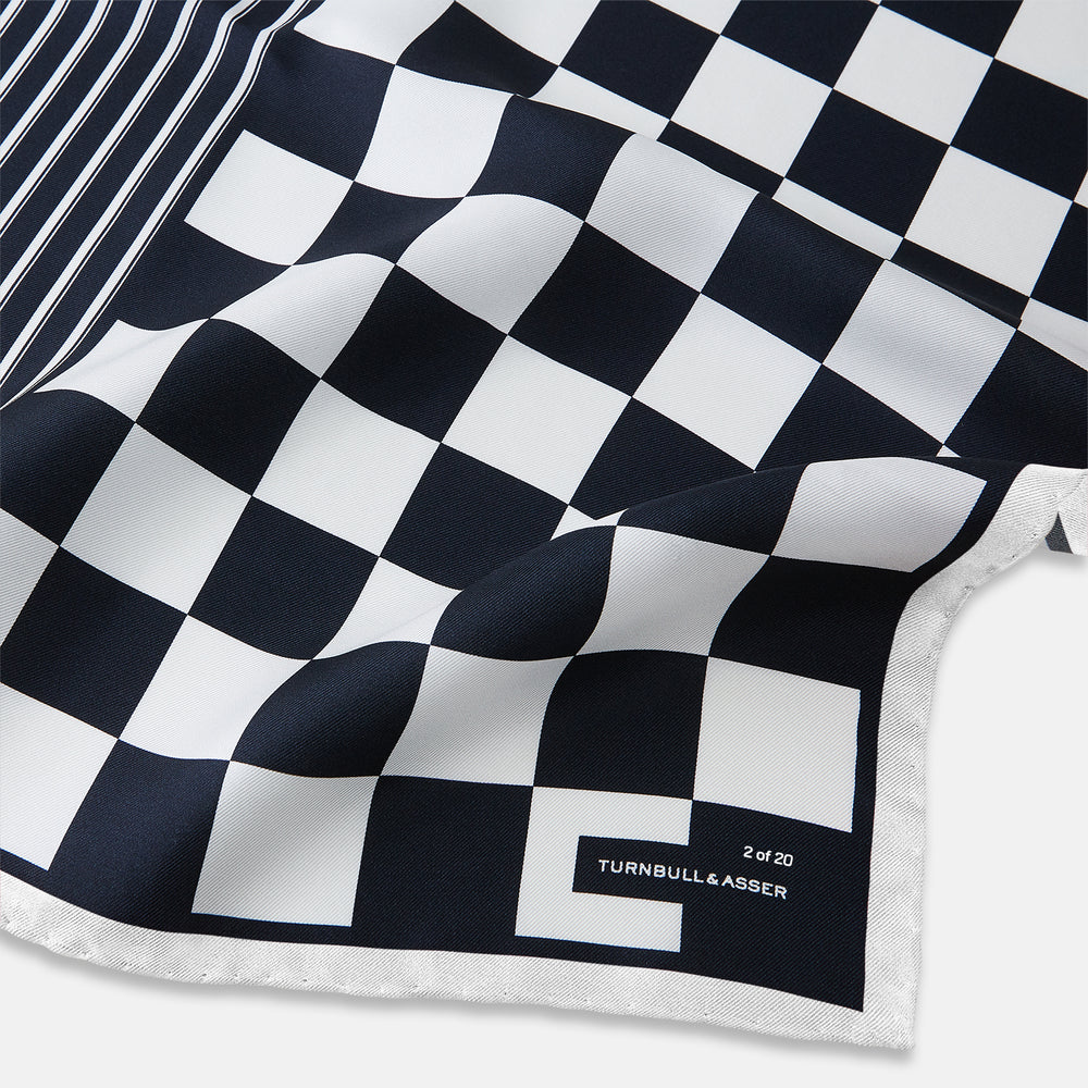 A square silk pocket square featuring a navy-on-white chequered pattern, labeled Turnbull & Asser UK with 2 of 20 in the bottom right corner—part of the limited edition Chequered Navy on White Frame Pocket Square from the Driver’s Capsule Collection.