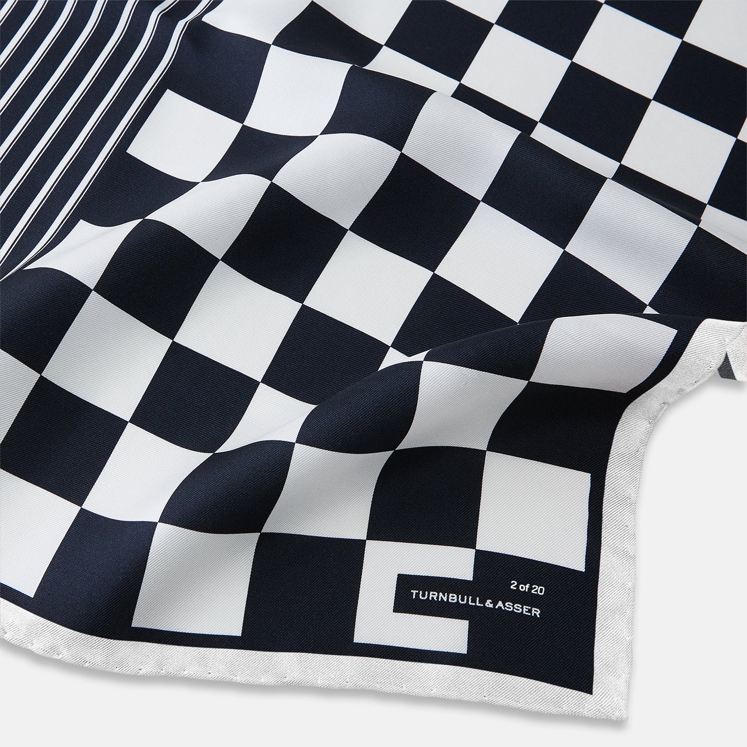 View 2 of product A square silk pocket square featuring a navy-on-white chequered pattern, labeled Turnbull & Asser UK with 2 of 20 in the bottom right corner—part of the limited edition Chequered Navy on White Frame Pocket Square from the Driver’s Capsule Collection.