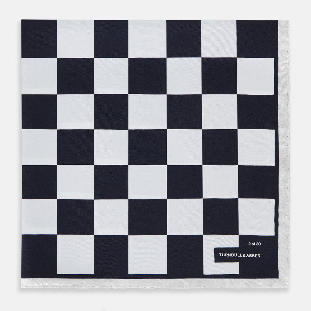A square silk pocket square featuring a navy-on-white chequered pattern, labeled Turnbull & Asser UK with 2 of 20 in the bottom right corner—part of the limited edition Chequered Navy on White Frame Pocket Square from the Driver’s Capsule Collection.