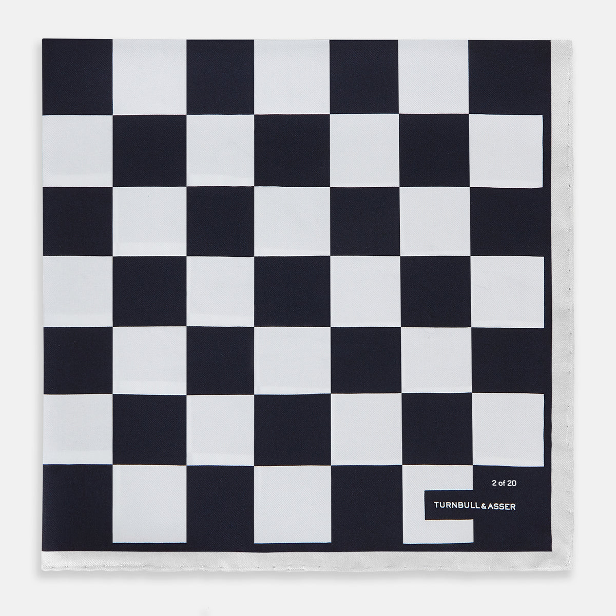 View 4 of product A square silk pocket square featuring a navy-on-white chequered pattern, labeled Turnbull & Asser UK with 2 of 20 in the bottom right corner—part of the limited edition Chequered Navy on White Frame Pocket Square from the Driver’s Capsule Collection.