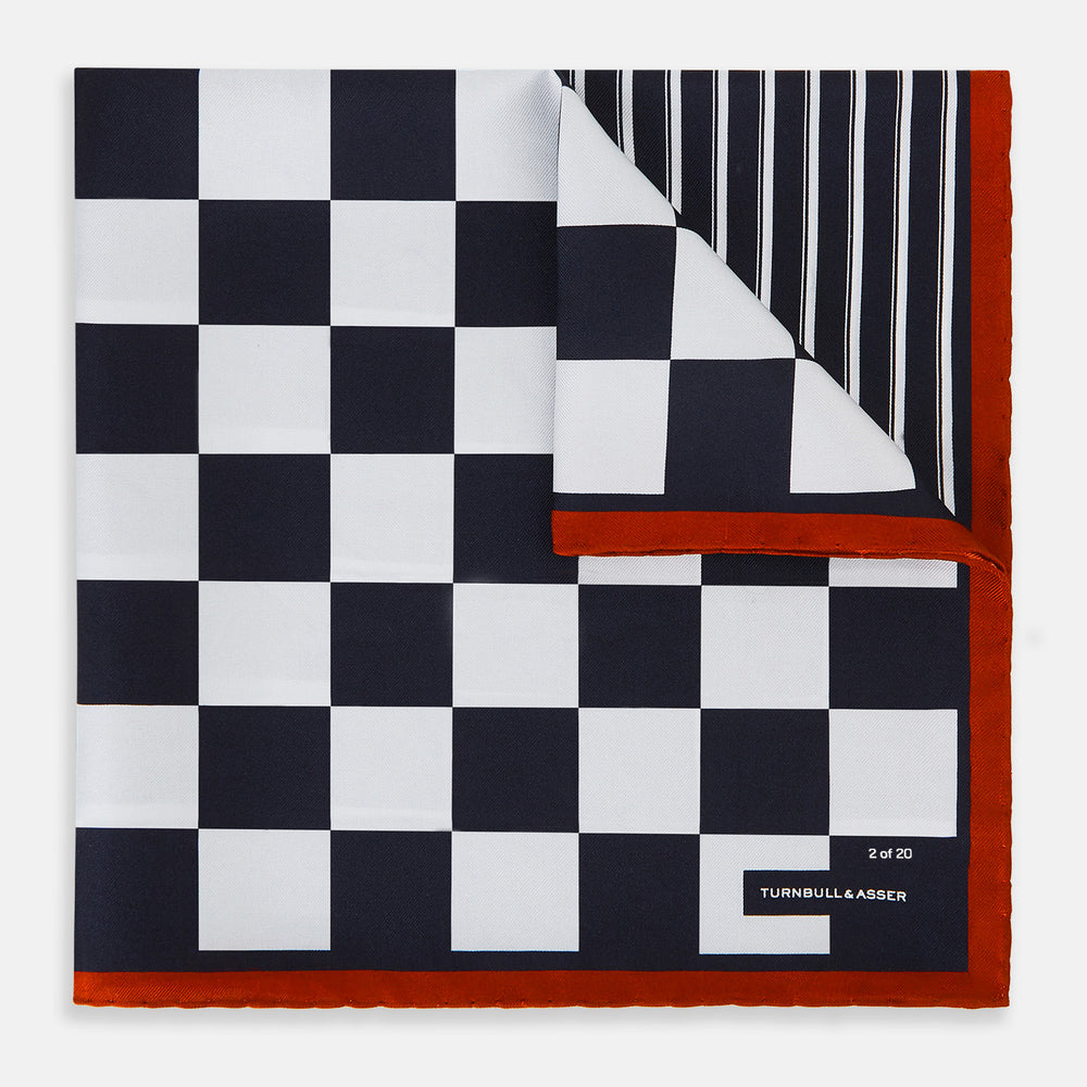 A limited edition silk pocket square from Turnbull & Asser UK, featuring a striking navy chequered pattern framed by a bold red border and finished with the text TURNBULL & ASSER in one corner. Part of the exclusive Driver’s Capsule Collection.