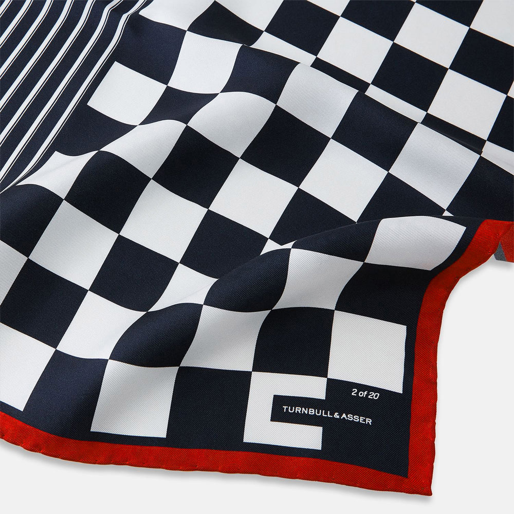 A limited edition silk pocket square from Turnbull & Asser UK, featuring a striking navy chequered pattern framed by a bold red border and finished with the text TURNBULL & ASSER in one corner. Part of the exclusive Driver’s Capsule Collection.