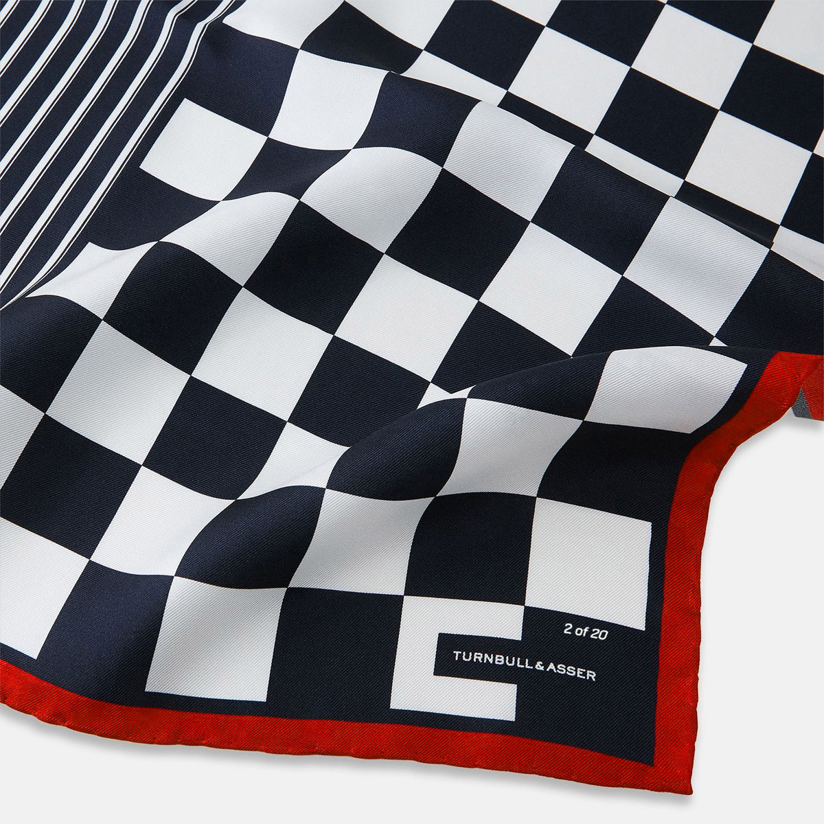 View 2 of product A limited edition silk pocket square from Turnbull & Asser UK, featuring a striking navy chequered pattern framed by a bold red border and finished with the text TURNBULL & ASSER in one corner. Part of the exclusive Driver’s Capsule Collection.