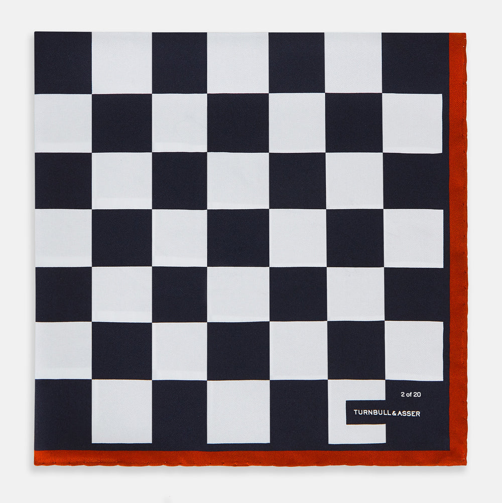 A limited edition silk pocket square from Turnbull & Asser UK, featuring a striking navy chequered pattern framed by a bold red border and finished with the text TURNBULL & ASSER in one corner. Part of the exclusive Driver’s Capsule Collection.