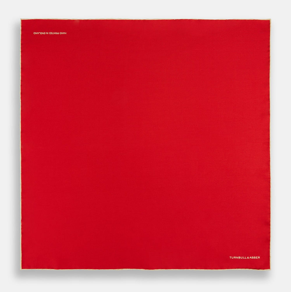 The Turnbull & Asser RED AND GOLD PIPED SILK POCKET SQUARE is a vibrant red silk accessory with gold edging and the brand’s logo in white on the bottom right—ideal for elevating formal looks.