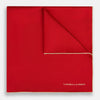 View 1 of product The Turnbull & Asser RED AND GOLD PIPED SILK POCKET SQUARE is a vibrant red silk accessory with gold edging and the brand’s logo in white on the bottom right—ideal for elevating formal looks.