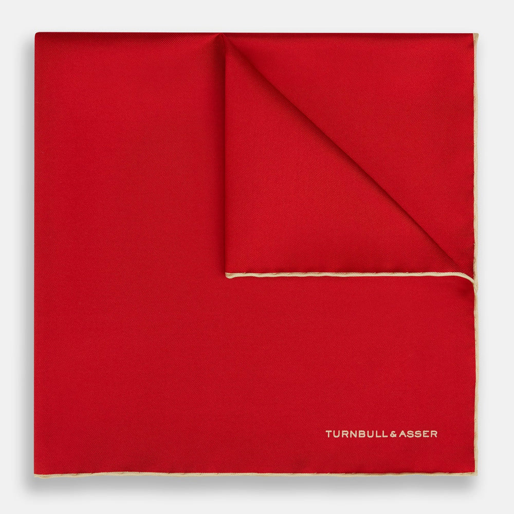 The Turnbull & Asser RED AND GOLD PIPED SILK POCKET SQUARE is a vibrant red silk accessory with gold edging and the brand’s logo in white on the bottom right—ideal for elevating formal looks.