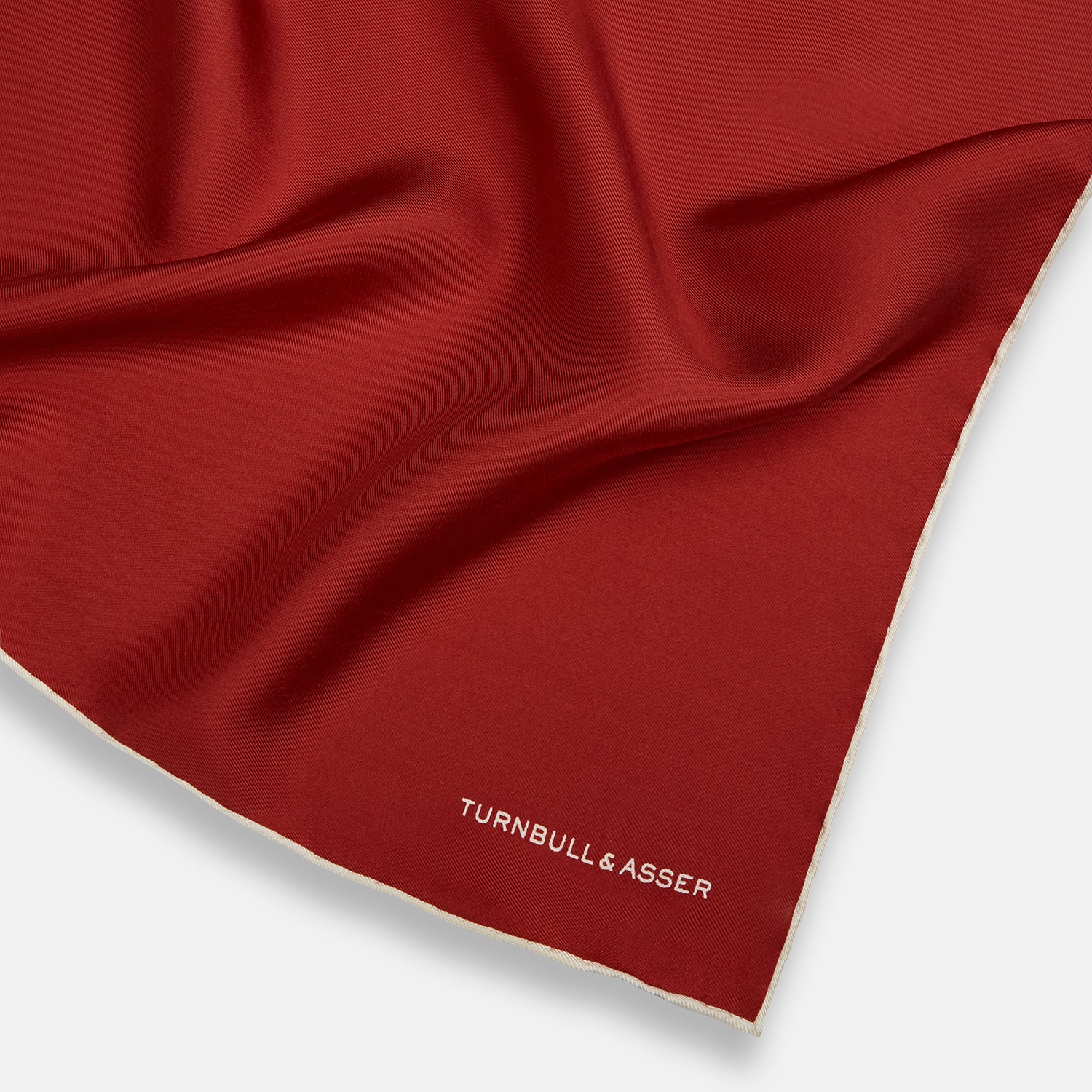 View 2 of product The Turnbull & Asser Burgundy and Ecru Piped Silk Pocket Square features a classic square design, contrasting ecru piping on the edge, and white branding in the lower corner—a refined accessory for formal looks.