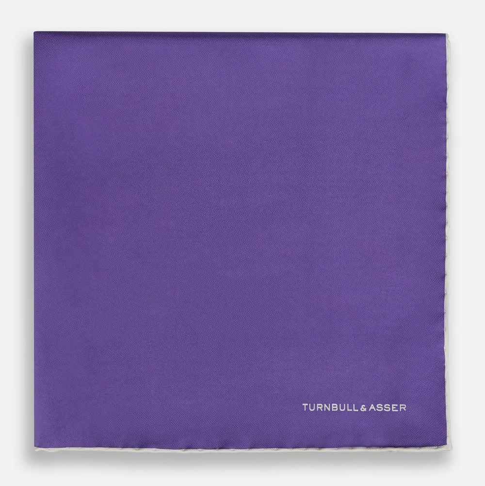 The Turnbull & Asser Violet and Ecru Piped Silk Pocket Square features a stitched edge and white brand logo, making it an elegant addition to formalwear.