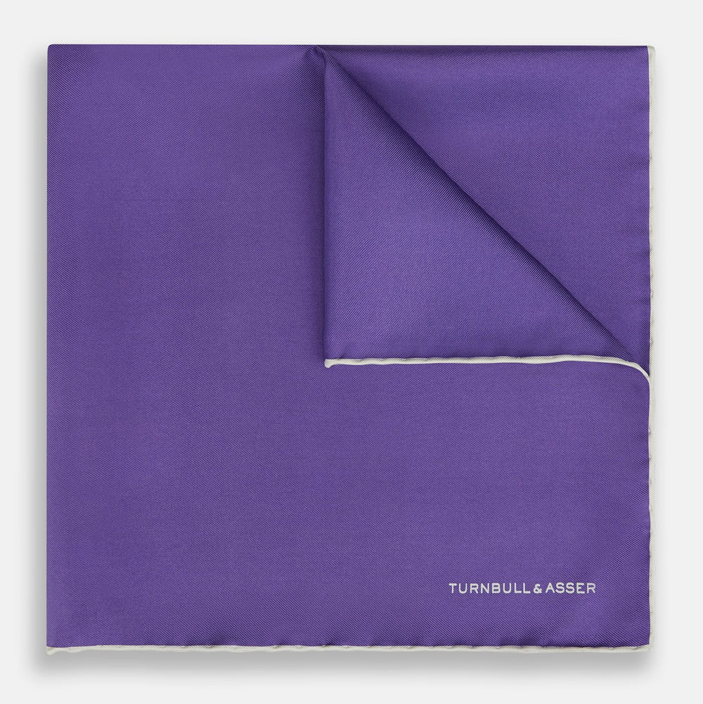 The Turnbull & Asser Violet and Ecru Piped Silk Pocket Square features a stitched edge and white brand logo, making it an elegant addition to formalwear.
