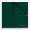 View 1 of product The FOREST GREEN AND ECRU PIPED SILK POCKET SQUARE by Turnbull & Asser features forest green silk with ecru piping, neatly folded to display both sides, and the brand name printed in white in the lower right corner—ideal for formal attire.