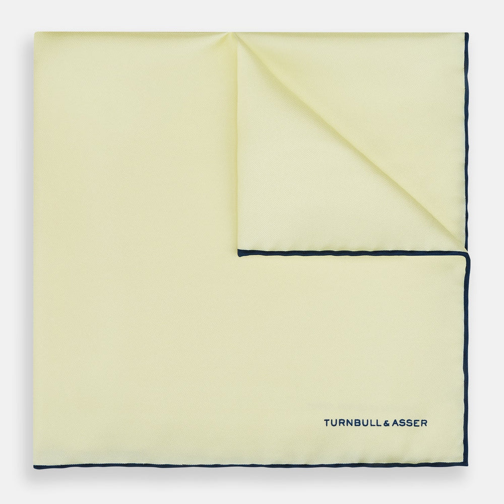 The Turnbull & Asser GOLD AND NAVY BLUE PIPED SILK POCKET SQUARE features navy piping and an embroidered logo—a refined accessory to elevate any formal look.