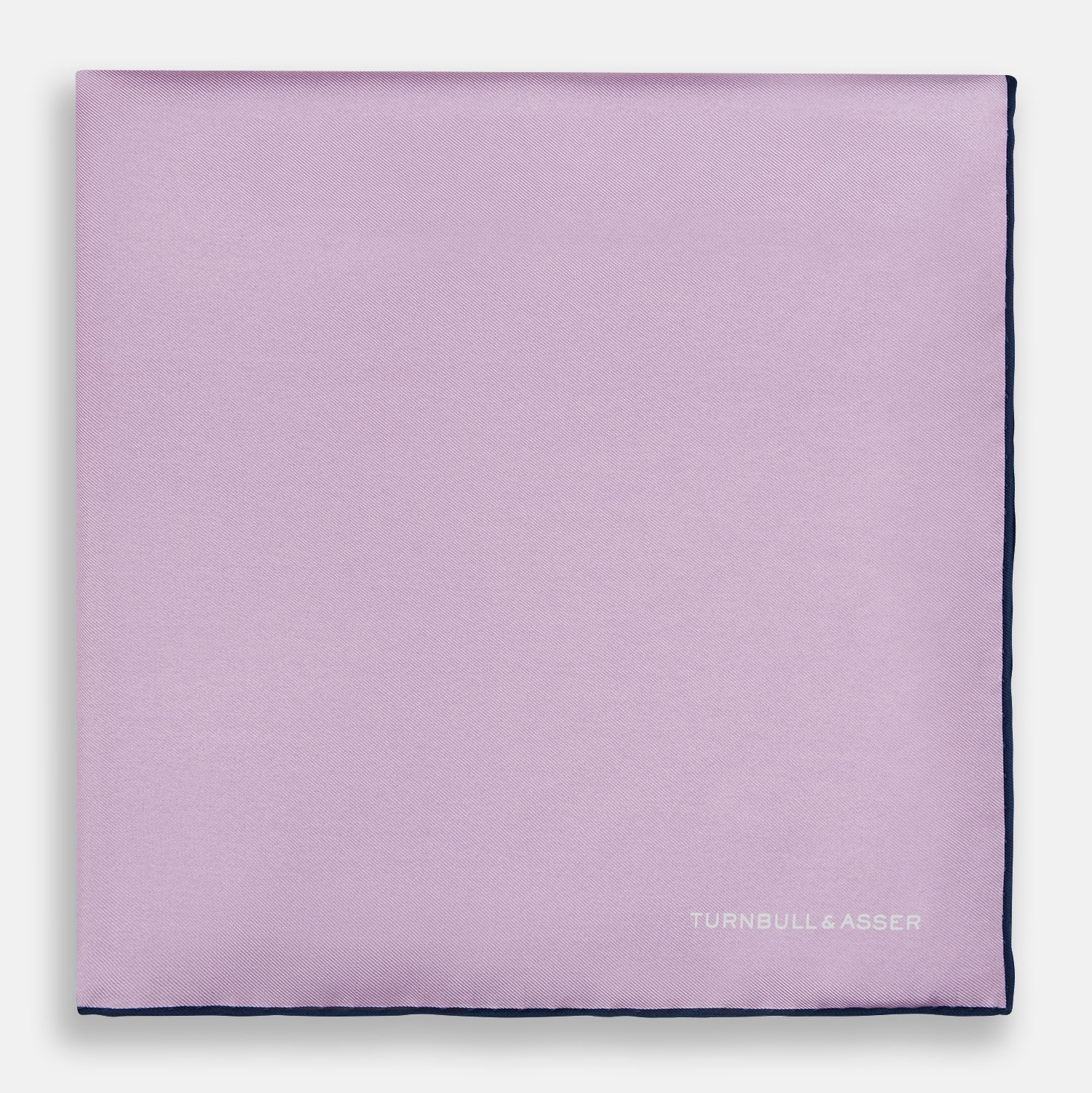 View 3 of product The Turnbull & Asser Lilac Piped Silk Pocket Square features dark edging and a white brand logo in one corner, making it a stylish choice for formal attire. Displayed against a white background.