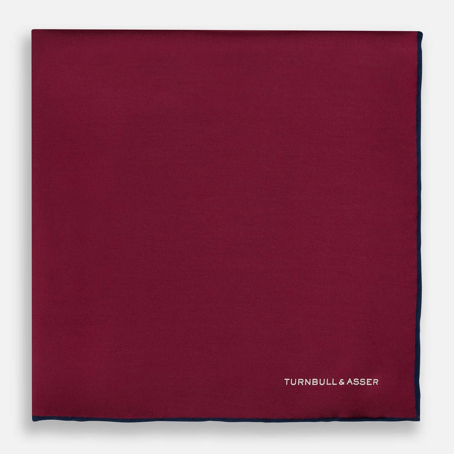 View 3 of product The Mauve Piped Silk Pocket Square by Turnbull & Asser features a dark blue edge and white embroidered logo in the lower right corner, making it ideal for formal occasions. Displayed on a plain white background.