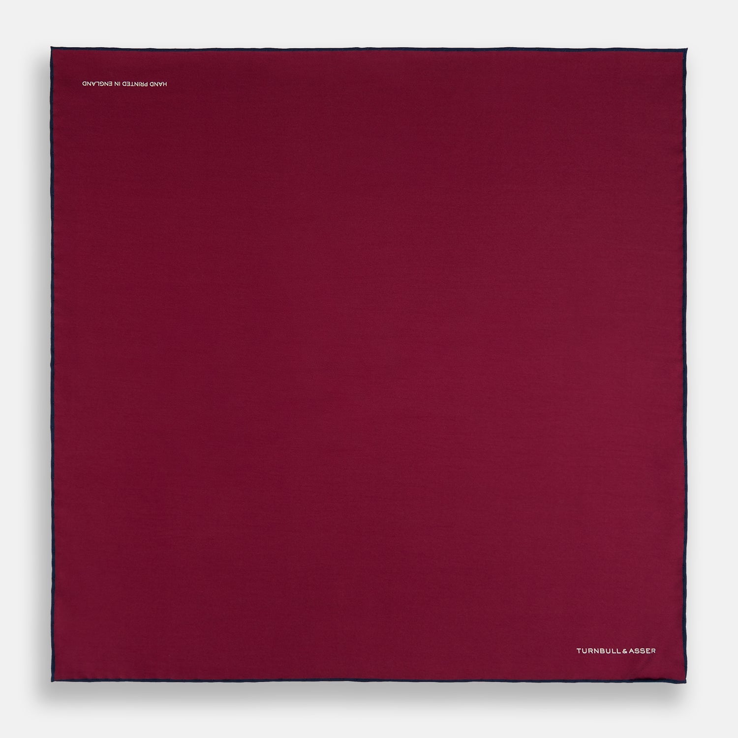 View 4 of product The Mauve Piped Silk Pocket Square by Turnbull & Asser features a dark blue edge and white embroidered logo in the lower right corner, making it ideal for formal occasions. Displayed on a plain white background.
