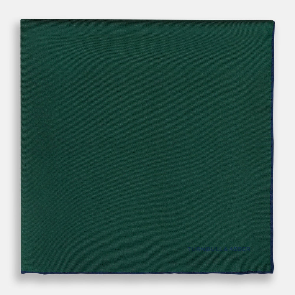 The Turnbull & Asser Petrol Green Piped Silk Pocket Square features a visible stitched edge and a discreet blue logo on the turned-down corner, adding an elegant accent to formal attire.