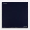 View 4 of product The Dark Blue Piped Silk Pocket Square by Turnbull & Asser features white piping, a one-corner fold revealing the underside, and the brand's name embroidered in white—perfect for formal occasions.