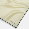 View 2 of product The Ecru and Navy Blue Piped Silk Pocket Square by Turnbull & Asser features contrasting navy piping and finely embroidered branding—an elegant finishing touch to any formal look.
