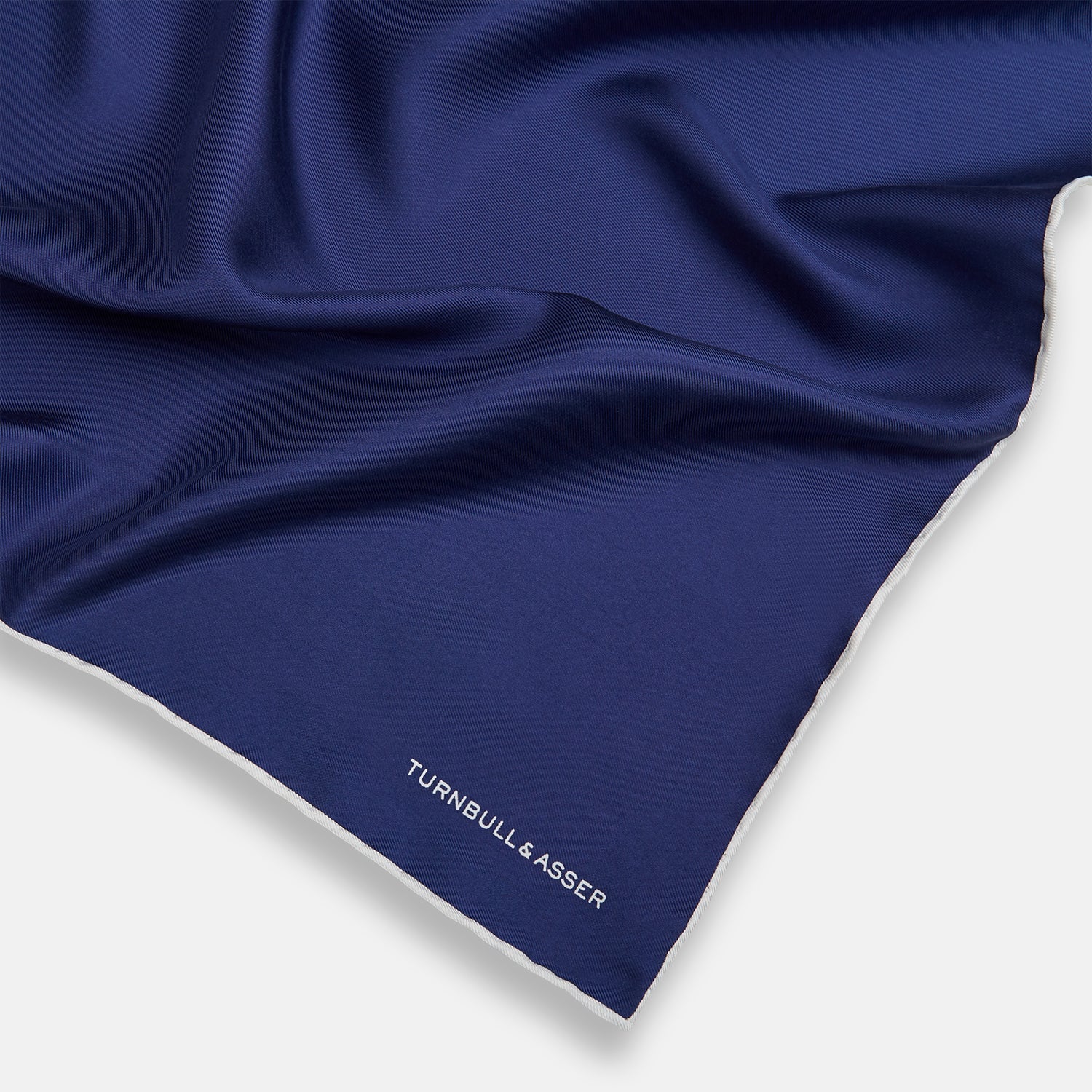 View 2 of product The Turnbull & Asser Mid Blue Piped Silk Pocket Square features a mid-blue hue with white edging, ideal for formal wear, and is finished with the brand’s name printed in white on the bottom right corner.