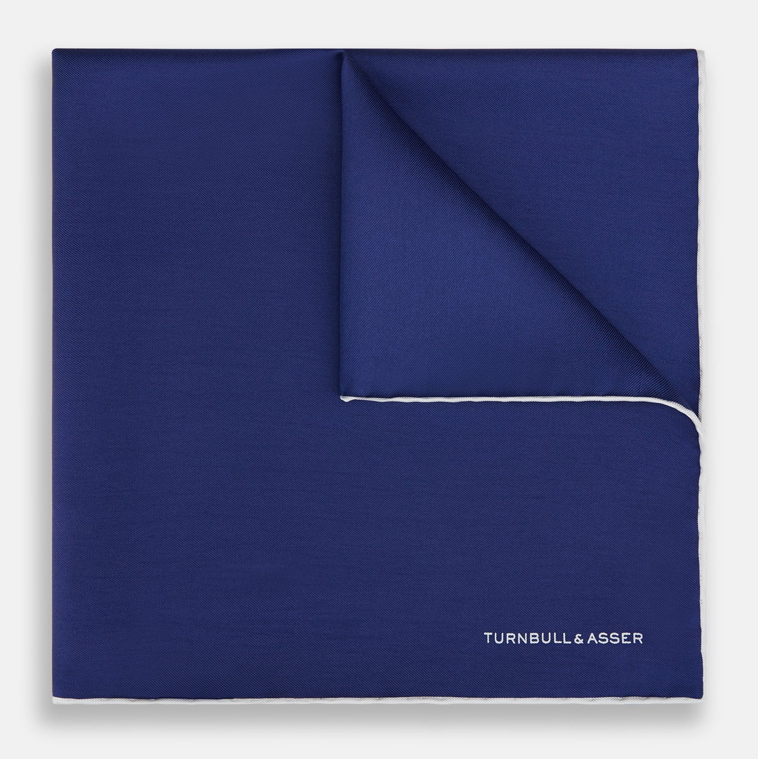 View 1 of product The Turnbull & Asser Mid Blue Piped Silk Pocket Square features a mid-blue hue with white edging, ideal for formal wear, and is finished with the brand’s name printed in white on the bottom right corner.