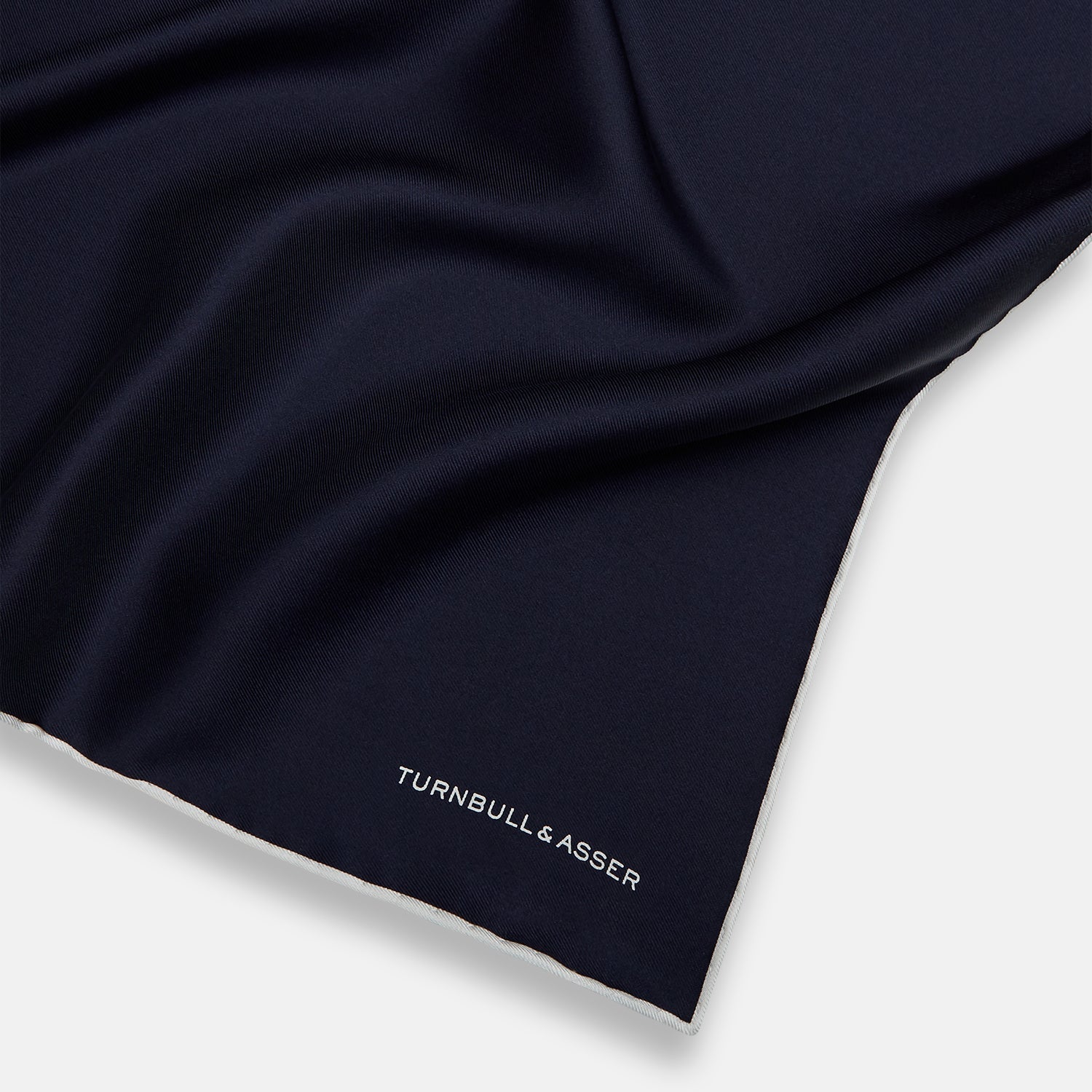 View 2 of product The Midnight Blue Piped Silk Pocket Square from Turnbull & Asser features crisp white trim and subtle branding, making it the ideal accessory to elevate your formal look.