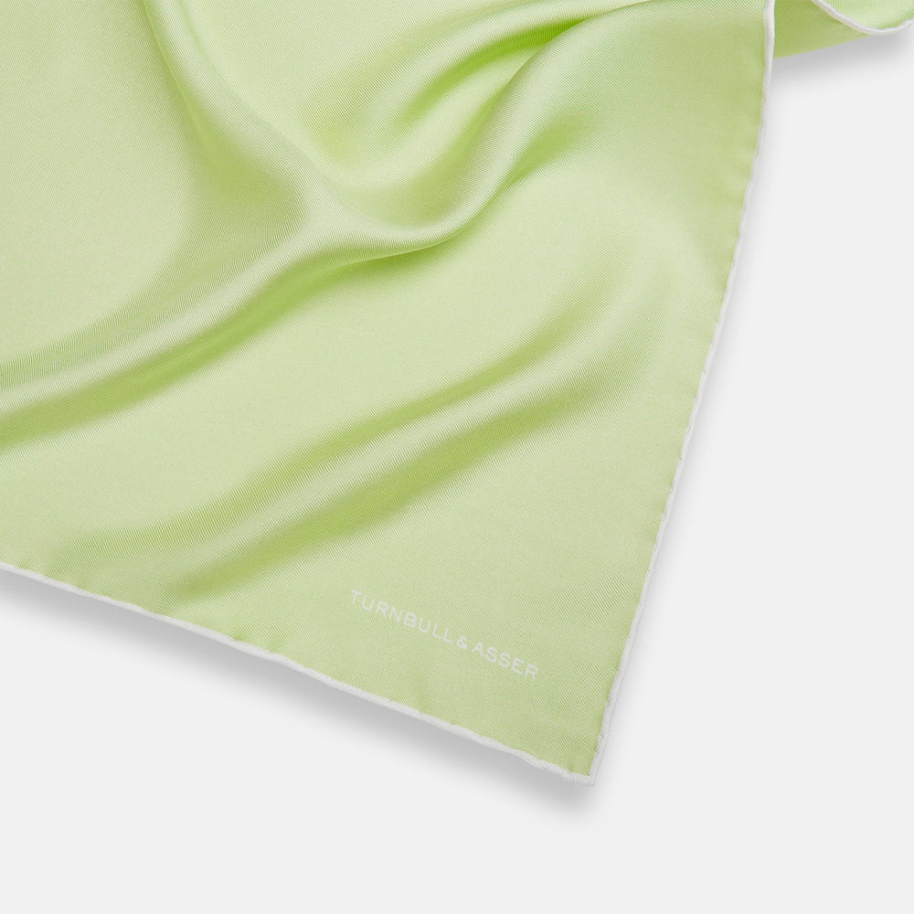 The Turnbull & Asser Mint and Ecru Piped Silk Pocket Square features a mint green silk fabric with subtle sheen and ecru piping, perfect for formal attire. "Turnbull & Asser" is embroidered in white in one corner.