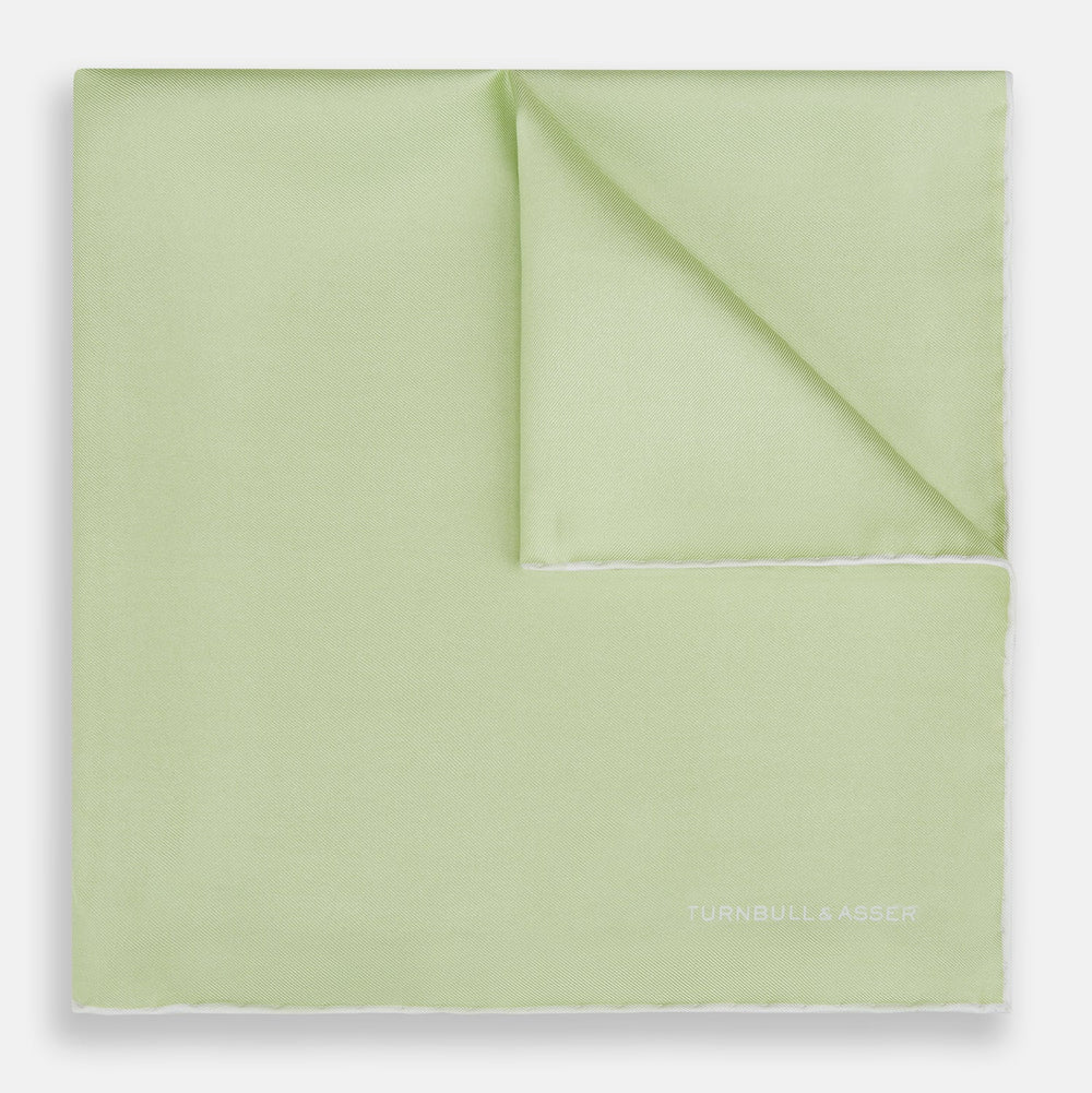 The Turnbull & Asser Mint and Ecru Piped Silk Pocket Square features a mint green silk fabric with subtle sheen and ecru piping, perfect for formal attire. "Turnbull & Asser" is embroidered in white in one corner.