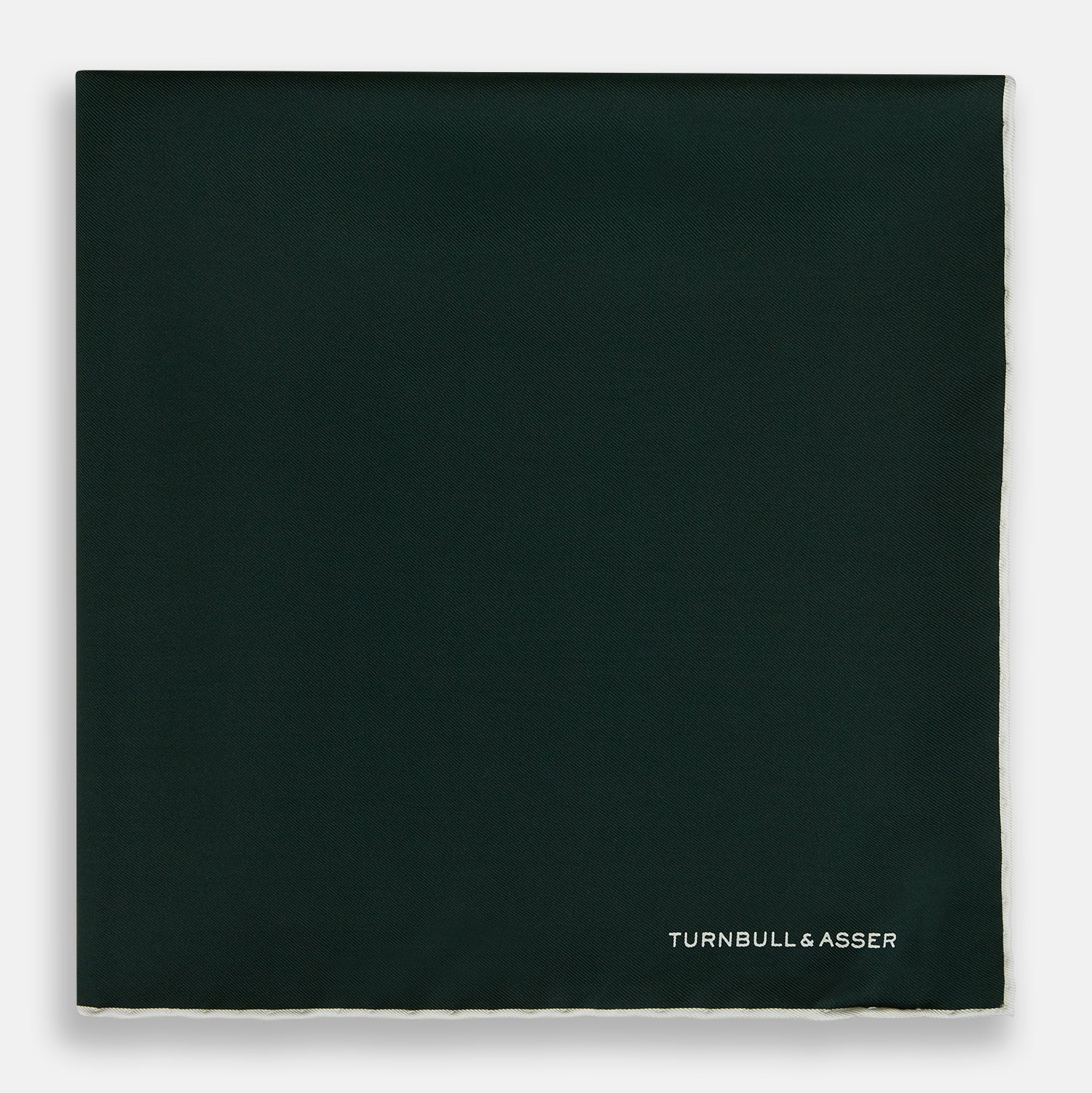 View 3 of product The DARK GREEN AND ECRU PIPED SILK POCKET SQUARE by Turnbull & Asser features ecru edging and the brand's logo in one corner, making it a refined choice for formal attire. One corner is folded to show the reverse side.