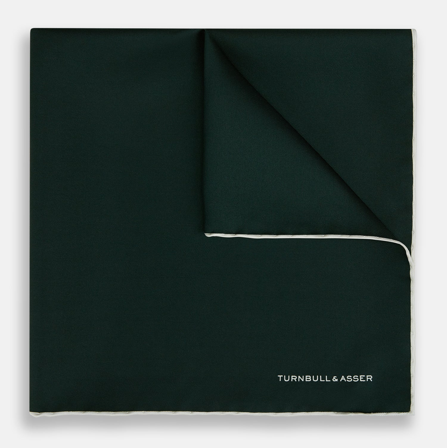 View 1 of product The DARK GREEN AND ECRU PIPED SILK POCKET SQUARE by Turnbull & Asser features ecru edging and the brand's logo in one corner, making it a refined choice for formal attire. One corner is folded to show the reverse side.