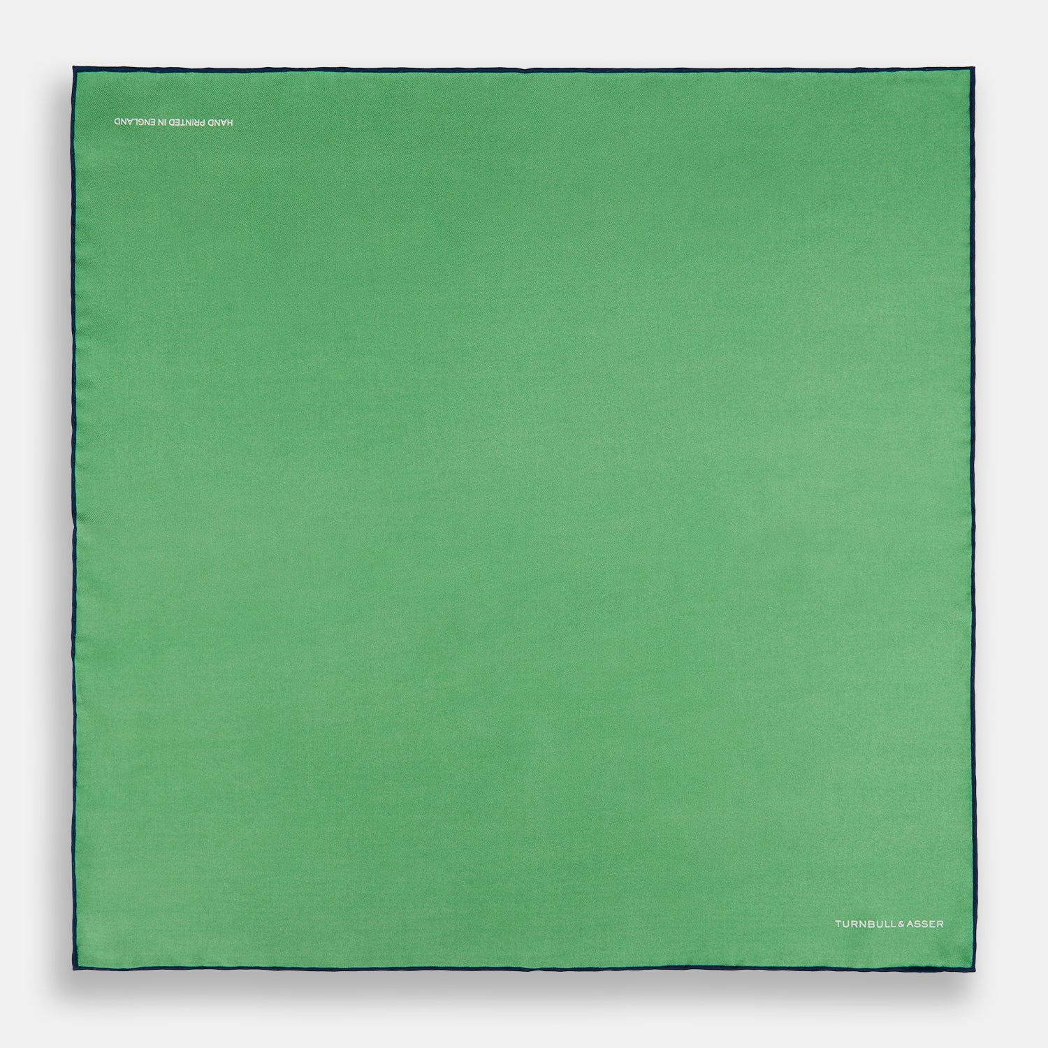 View 4 of product The Fern Green Piped Silk Pocket Square by Turnbull & Asser features a dark blue edge and white embroidered branding at the corner—an elegant accessory for formal wear.