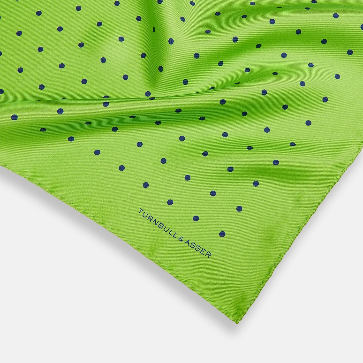 View 2 of product The Turnbull & Asser Lime Green and Blue Spot Silk Pocket Square features evenly spaced blue dots and the brand’s text in the bottom right corner. One corner is folded to reveal the reverse, making it ideal for formal occasions.
