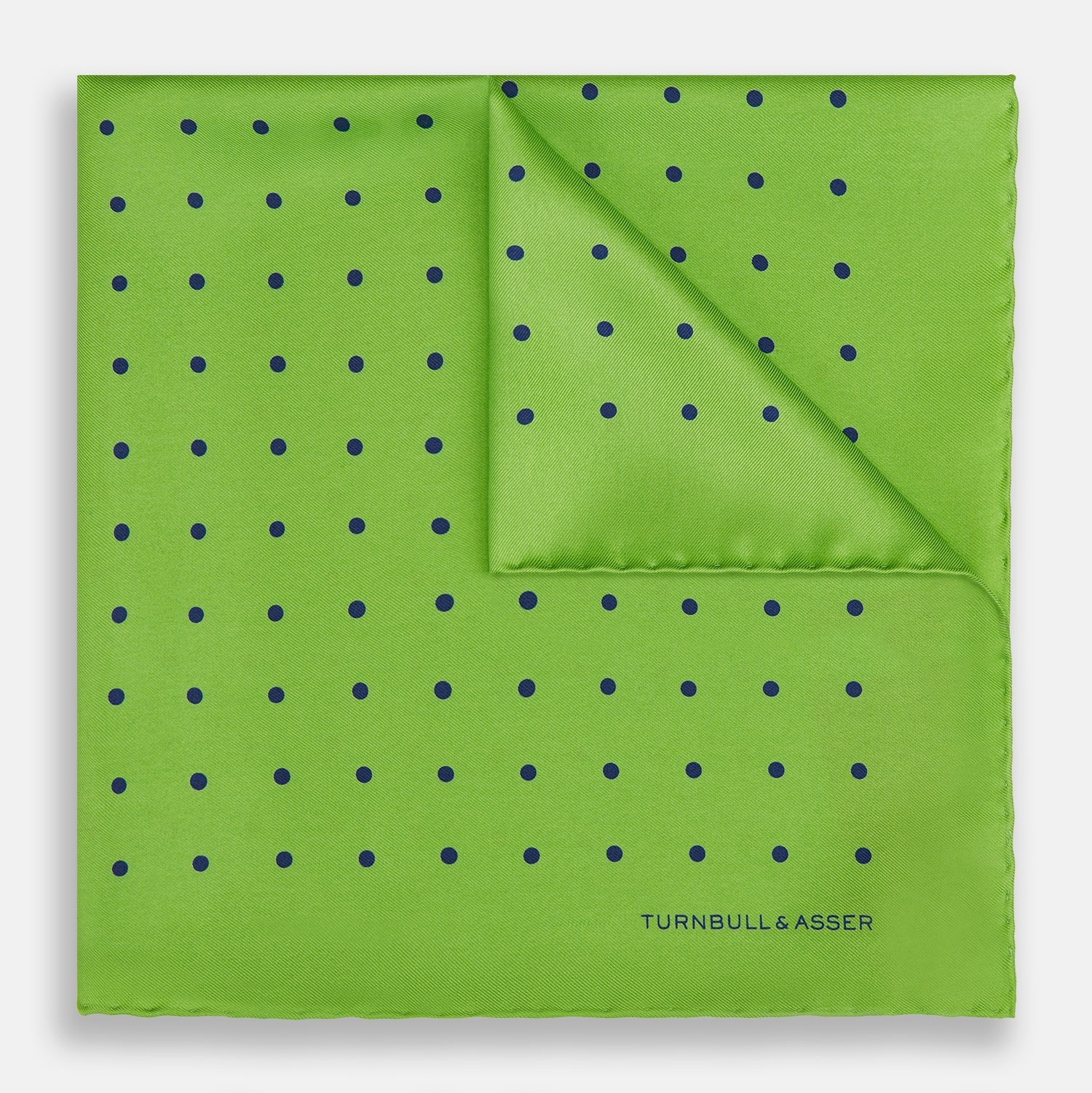 View 1 of product The Turnbull & Asser Lime Green and Blue Spot Silk Pocket Square features evenly spaced blue dots and the brand’s text in the bottom right corner. One corner is folded to reveal the reverse, making it ideal for formal occasions.