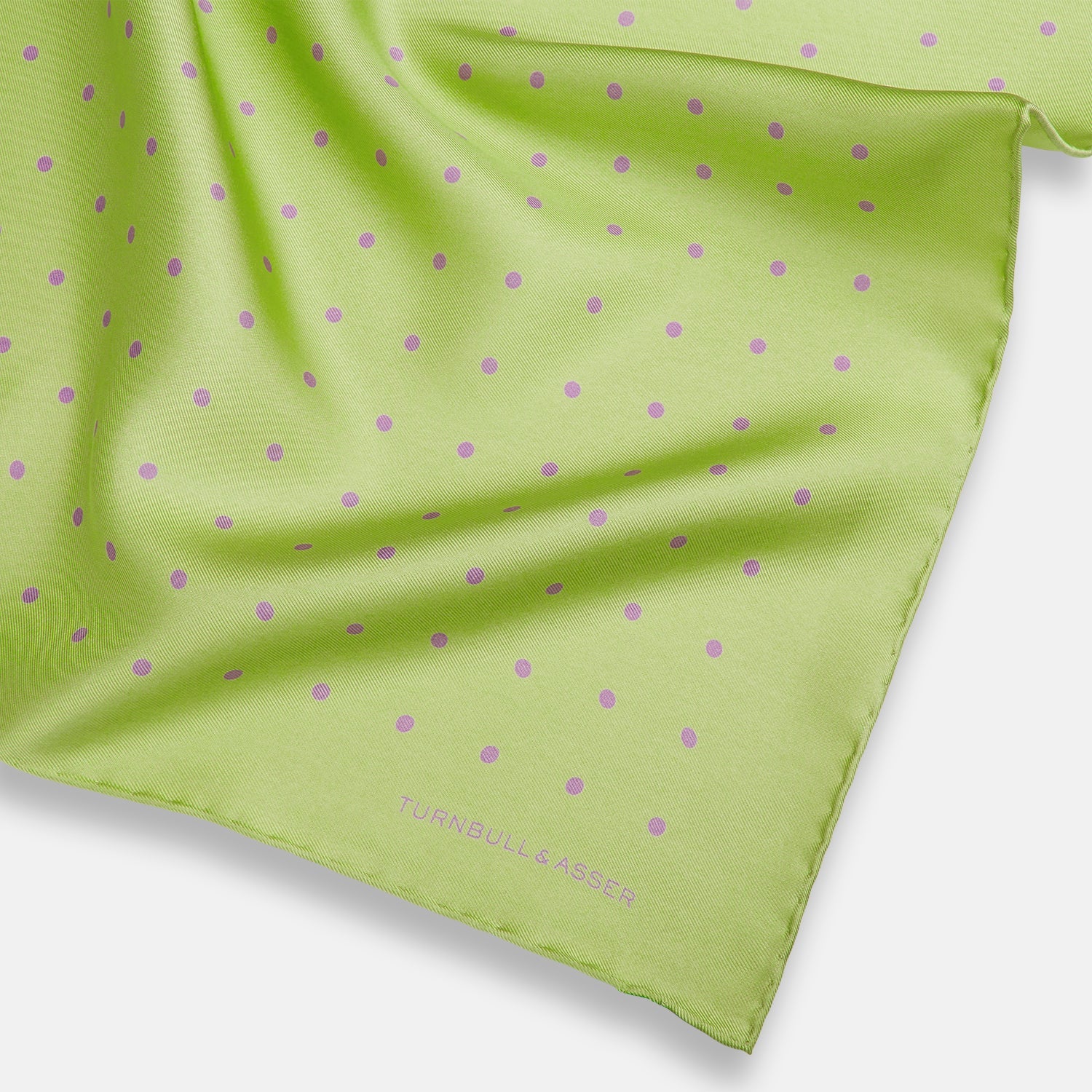 View 2 of product The Turnbull & Asser Melon Green and Lilac Spot Silk Pocket Square features evenly spaced lilac dots and the brand's name in one corner—a refined accessory for formal attire.